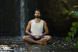 Person meditating in a serene forest setting with a waterfall, symbolizing the transformative power of meditation